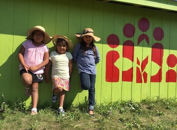 Jayla, Jaelie and Kaylie from Waywayseecappo First Nation learn against a green, wooden wall with the CFTC logo printed on it.