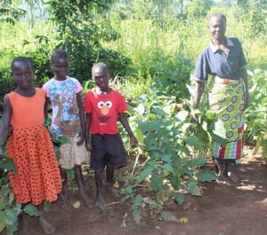 Mary smiles with her grandchildren in front of crops