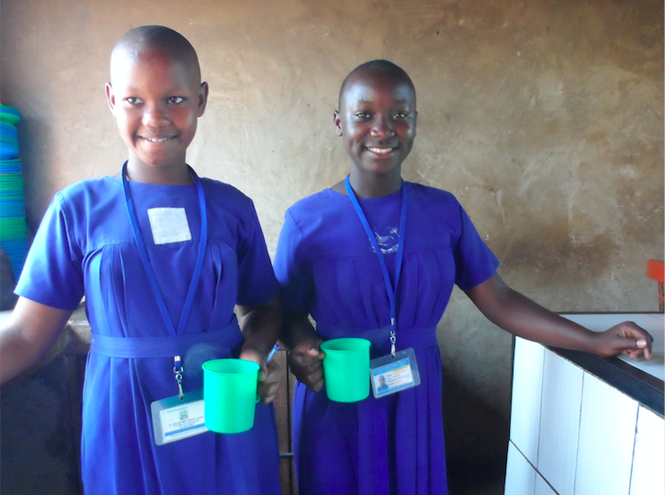 two Ugandan girls standing in a kitchen holding green cups